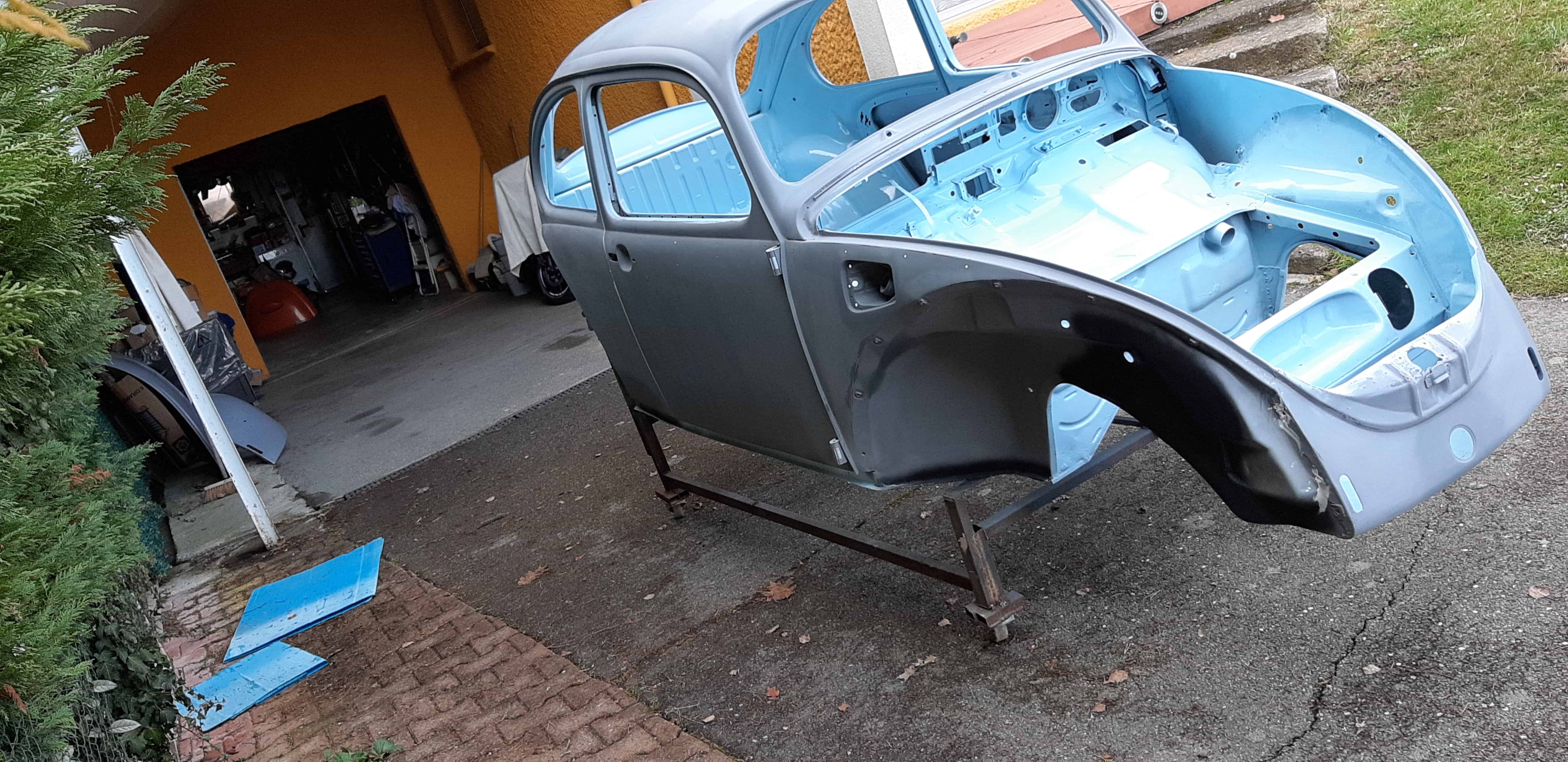 Caisse de Coccinelle mise à nu et passée en apprêt, posée sur un chariot de restauration devant un garage