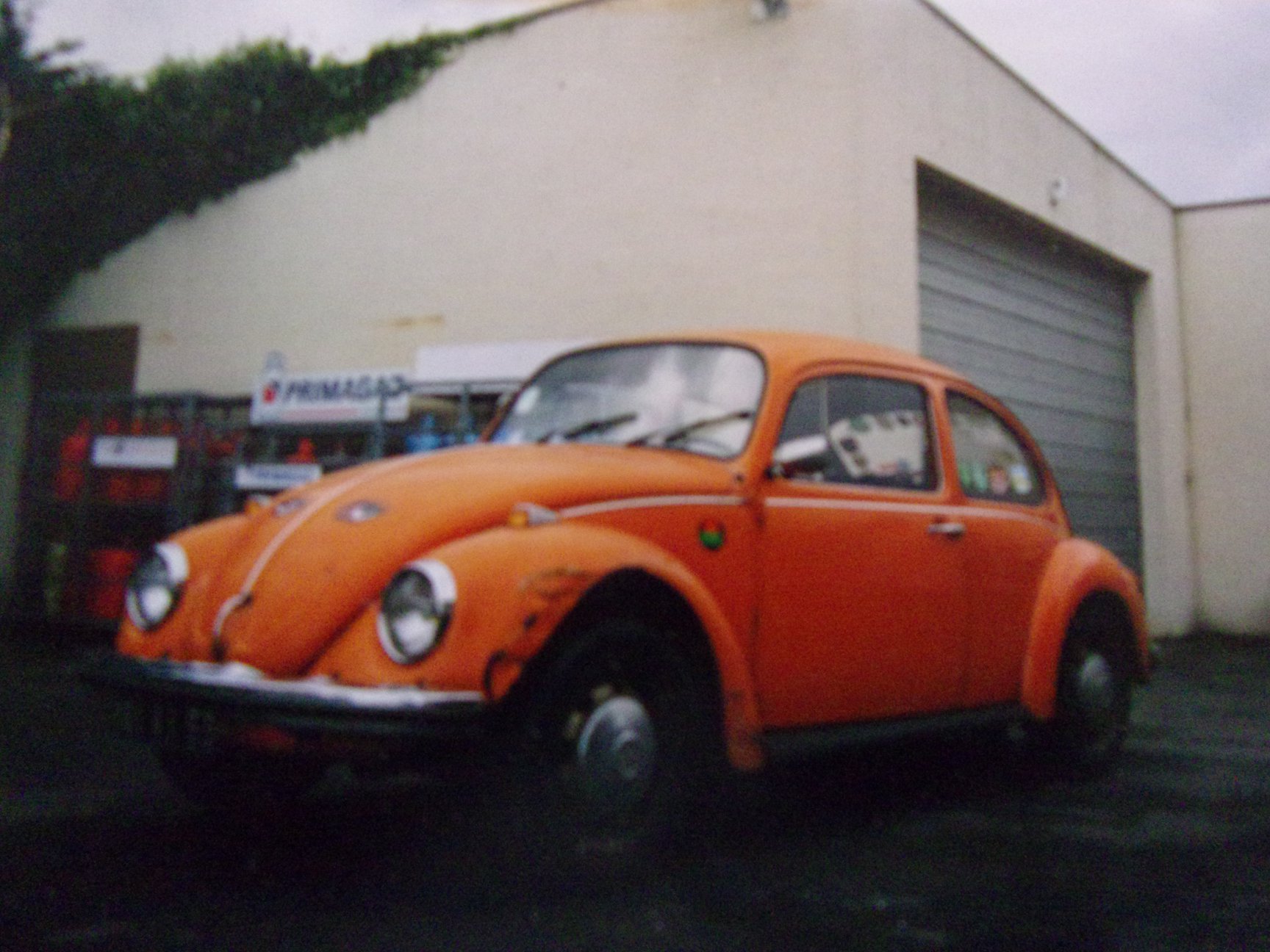Coccinelle 1200 orange de 1974 dans son jus, avant restauration, garée devant un bâtiment