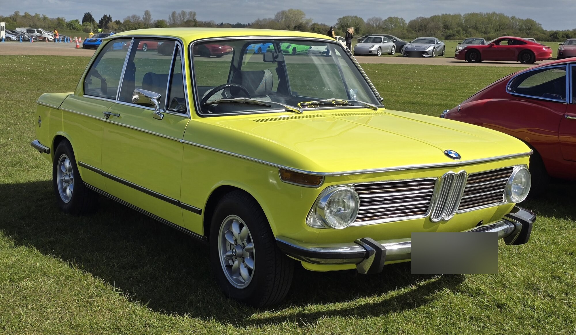 BMW 2002 tii jaune de 1973 vue de trois quarts avant, garée sur l'herbe lors d'un rassemblement de voitures