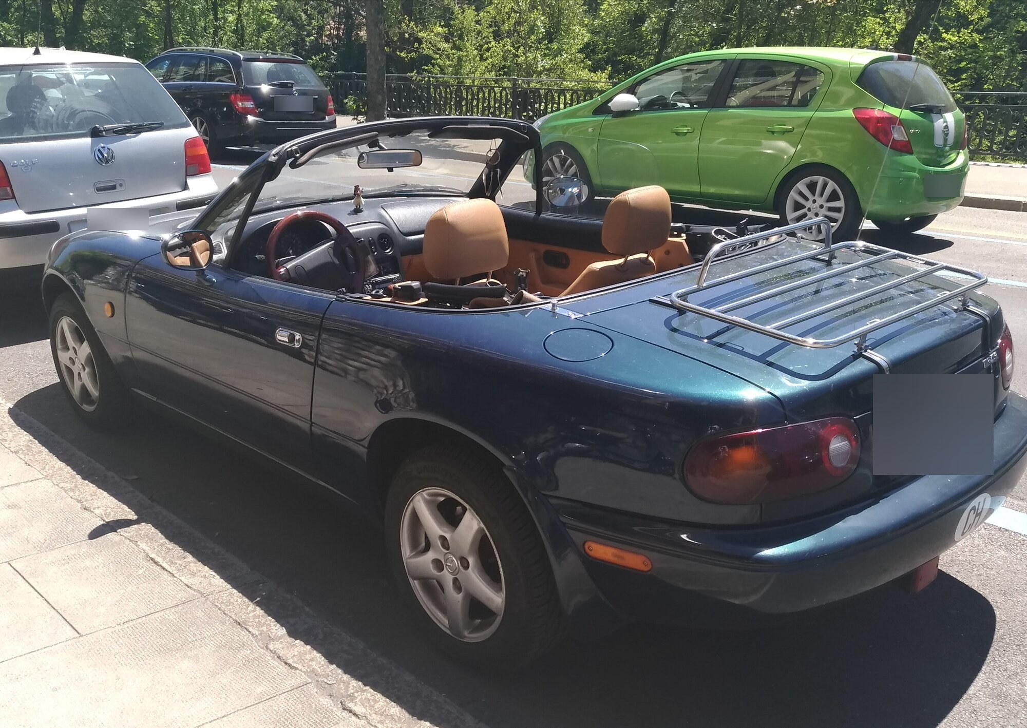 Mazda MX-5 NA vert foncé décapotée vue de trois quarts arrière, sellerie cuir fauve et porte-bagages chromé sur le coffre