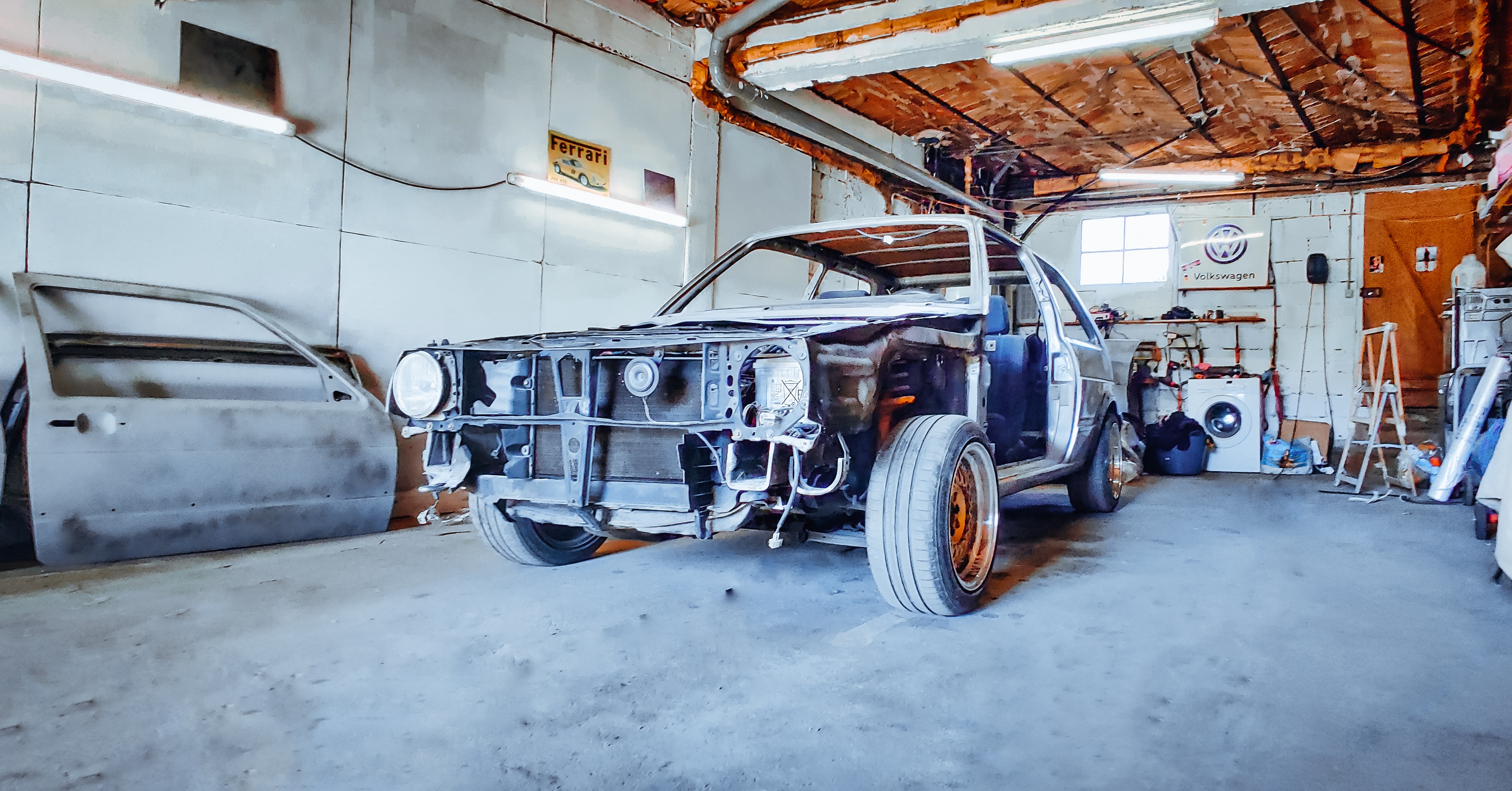 Golf 2 en cours de restauration dans un atelier : face avant déposée, caisse mise à nu, portière posée contre le mur