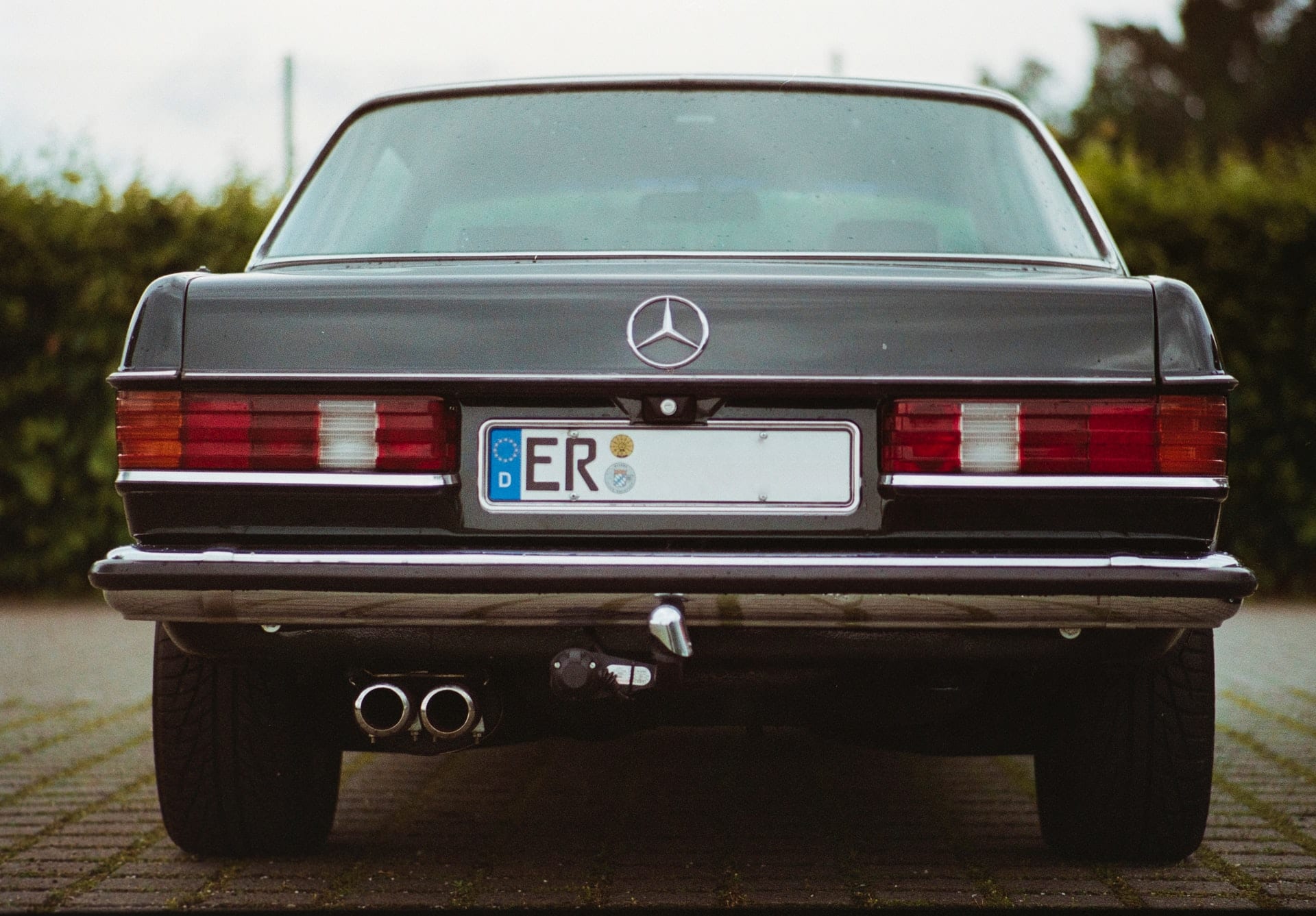 Arrière d'une berline Mercedes W123 de couleur sombre, avec ses feux horizontaux et son étoile au centre du coffre