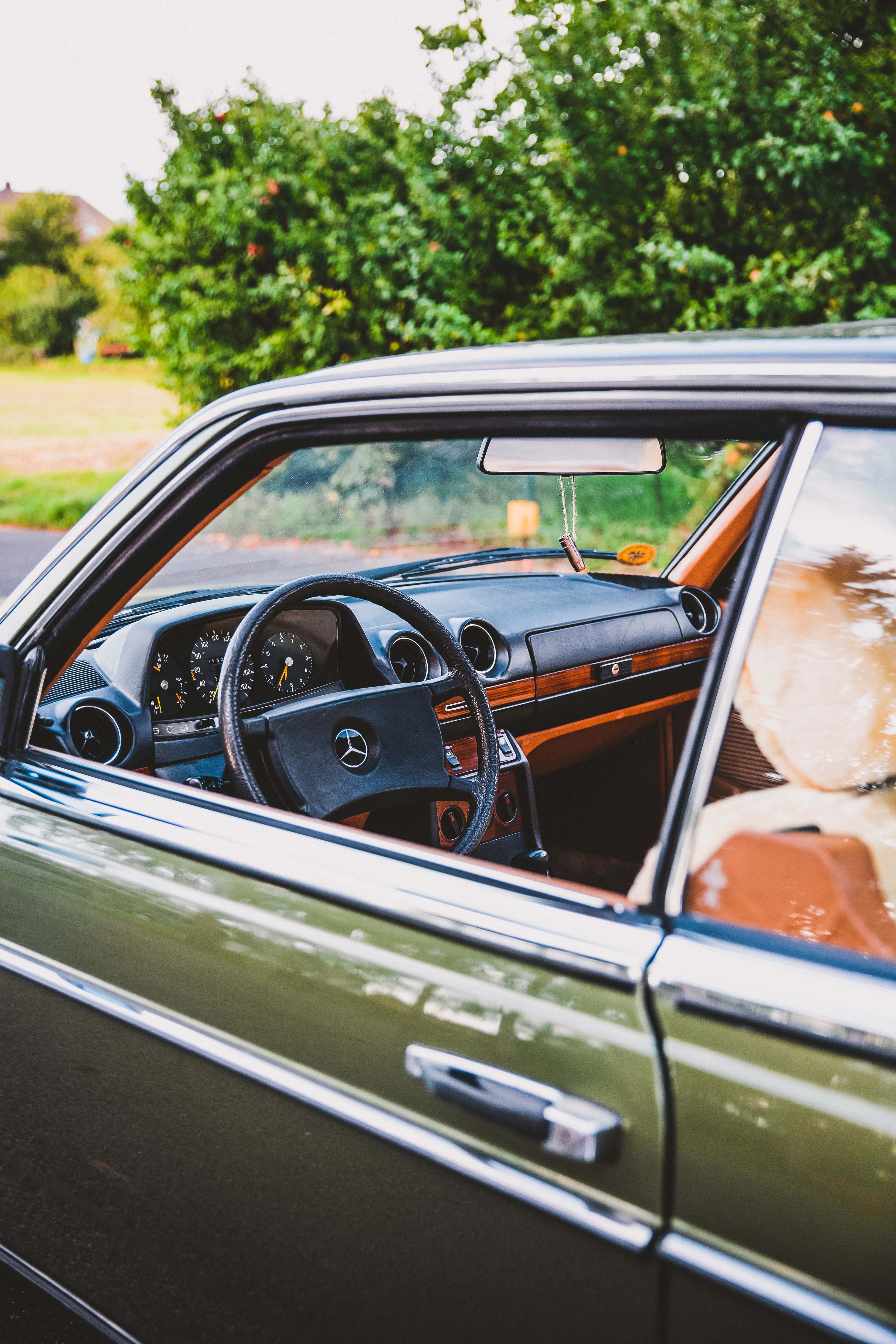 Habitacle d'une Mercedes W123 vu par la vitre conducteur : volant à quatre branches, planche de bord noire et inserts en bois