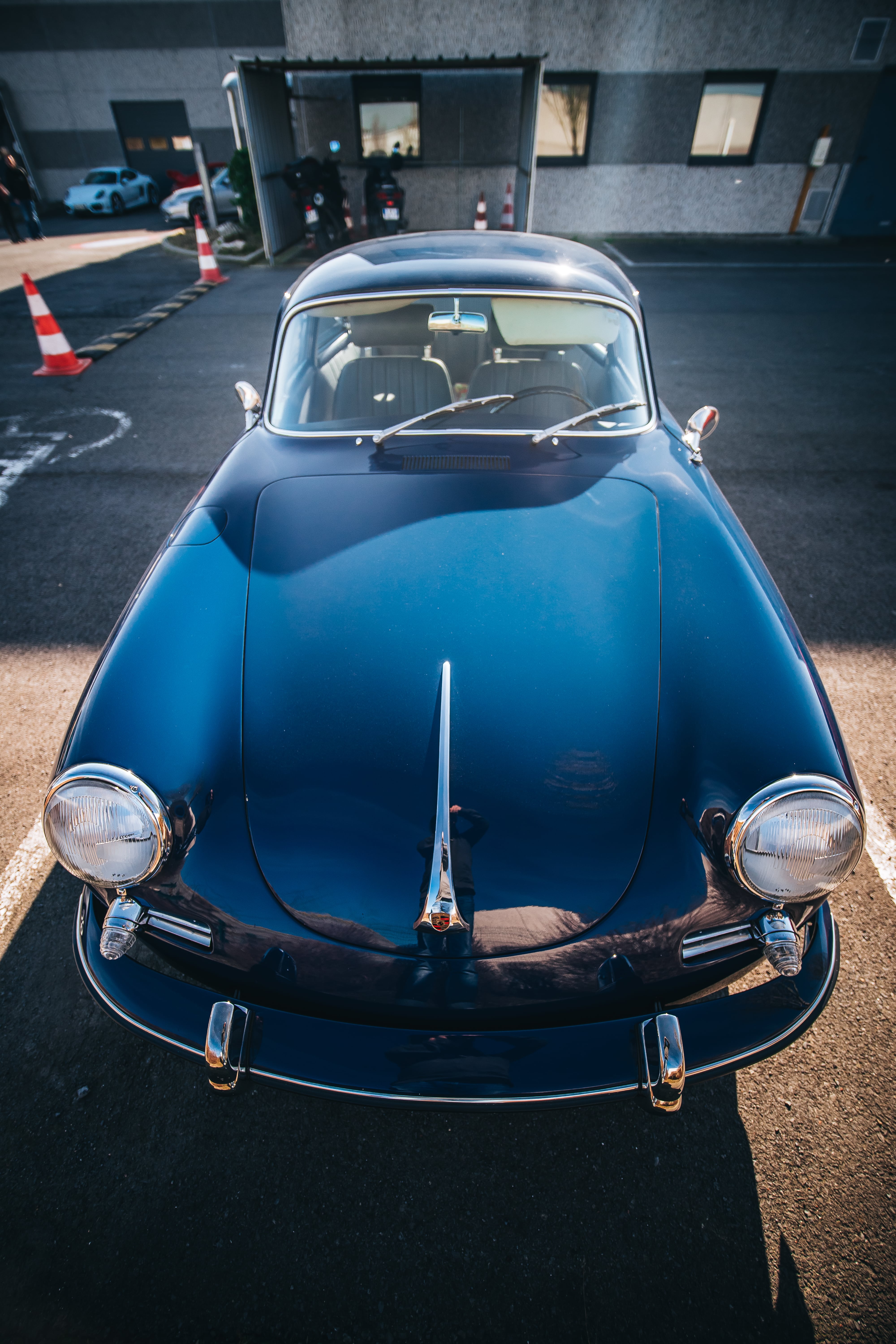 Porsche 356 C coupé bleu nuit vue de face en plongée, capot avant bombé, phares ronds et butoirs de pare-chocs chromés