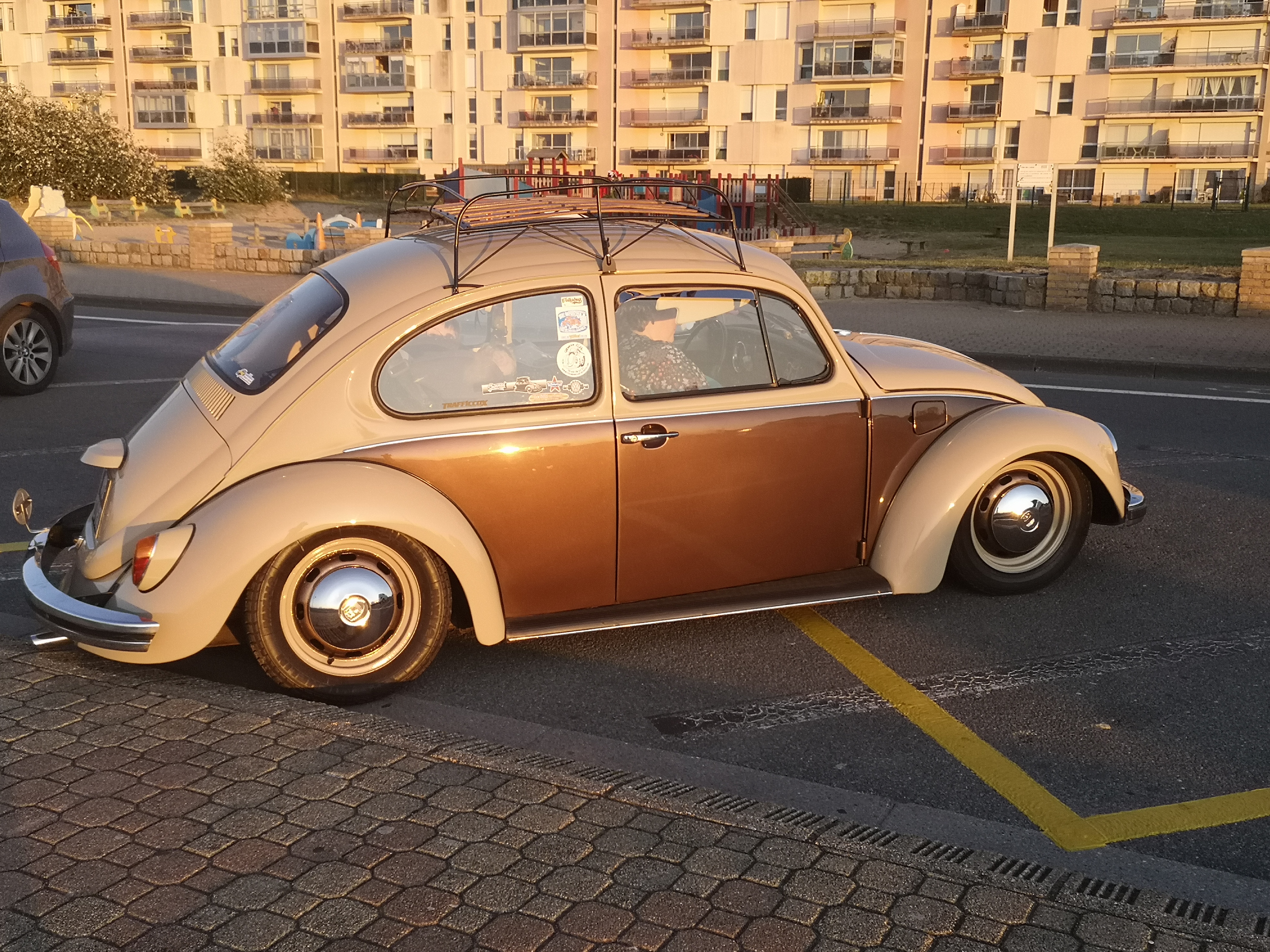 Coccinelle de 1975 bicolore crème et brun, galerie de toit chargée, vue de profil au soleil couchant